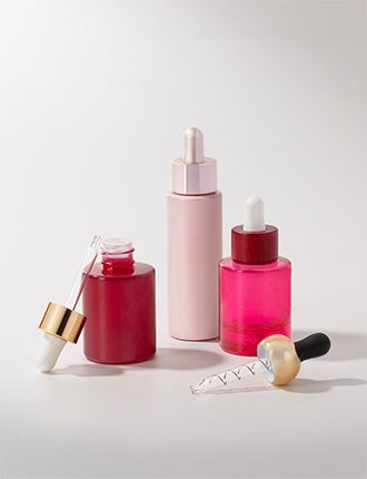 Collection of pink and reddish cosmetic containers with various droppers in different finishes—matte, glossy, gold, and colored—displayed on a grey background.