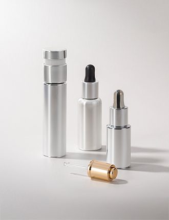 A collection of silver and gold cosmetic containers with various dispensing mechanisms, including droppers and pumps, displayed on a neutral background.