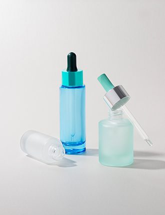 Collection of molded glass containers in various sizes, shapes, and finishes—some matte, others transparent, and some glossy—with different push-button dispensing mechanisms, displayed on a grey background.