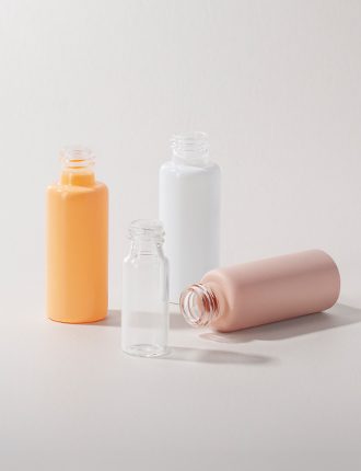 Collection of tubular glass bottles in various sizes, colors, and finishes displayed on a gray-colored background.