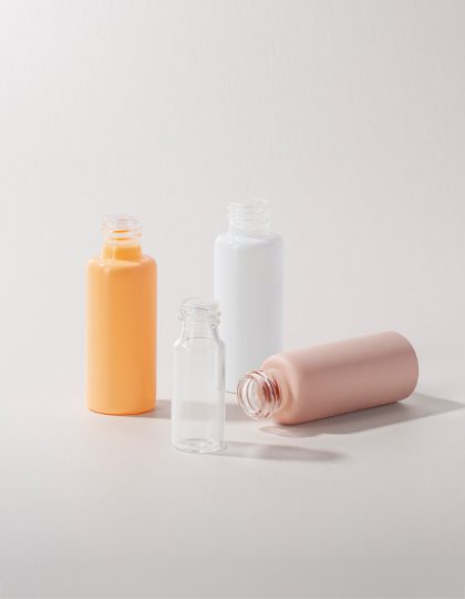 Collection of tubular glass bottles in various sizes, colors, and finishes displayed on a gray-colored background.